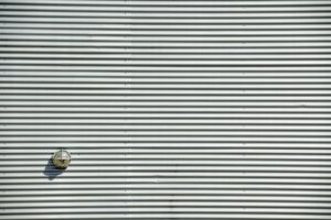 Corrugated metal wall featuring a round light fixture casting a shadow. Perfect industrial background.