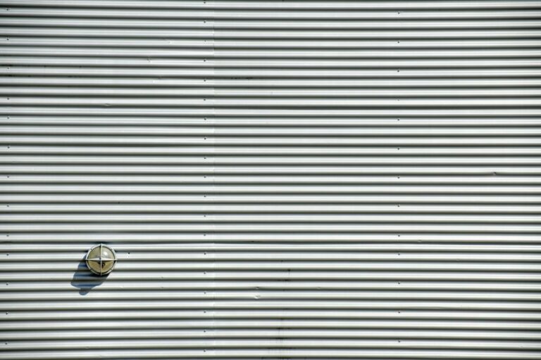 Corrugated metal wall featuring a round light fixture casting a shadow. Perfect industrial background.
